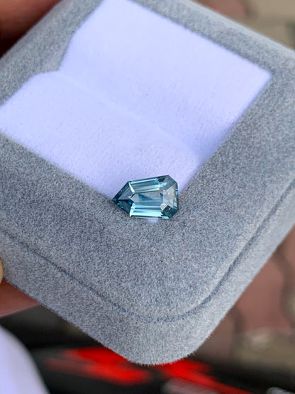 Le Saphir Teal de 1,65 carat de Bonnot Paris est présenté dans un écrin gris clair à l'intérieur blanc. Sa forme asymétrique aux multiples surfaces réfléchissantes met en valeur sa clarté et sa couleur sur un fond flou.