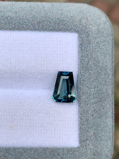 Un Saphir Teal facetté (2,52 ct) de Bonnot Paris avec une taille inhabituelle repose sur une surface blanche et coussinée dans un cadre rectangulaire gris, réfléchissant la lumière pour mettre en valeur sa clarté et sa couleur avec une élégance exceptionnelle.