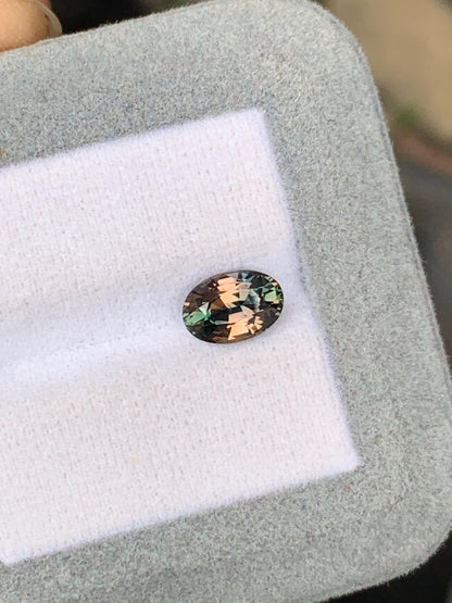 Un Saphir bicolore ovale étincelant de 2,05 ct de Bonnot Paris, aux reflets verts et roses, repose sur un support gris clair. Originaire du Sri Lanka, cette pierre précieuse reflète magnifiquement la lumière pour mettre en valeur ses facettes complexes.