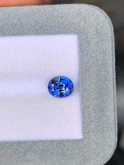 Le Saphir bicolore • 2,10ct de [NOUVEAU] Bonnot Paris, un exquis saphir bleu ovale du Sri Lanka, est magnifiquement mis en valeur sur une surface en tissu blanc et gris.