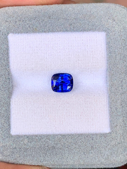 Un saphir bleu taille coussin de 2,03 carats du Sri Lanka par Bonnot Paris repose sur un tissu blanc dans une boîte à bijoux grise.