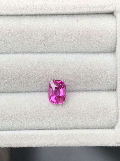 Un Saphir rose éclatant de 2,10 carats, taille coussin, signé Bonnot Paris, repose dans un écrin gris clair strié. Ses facettes captent la lumière, révélant de multiples nuances de rose.