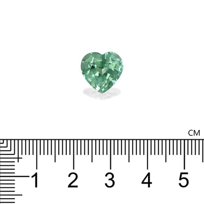 Une Tourmaline Verte en forme de cœur de 5,65 ct de Bonnot Paris repose sur une surface blanche, avec une règle noire en centimètres en dessous indiquant que la pierre précieuse mesure environ 1,5 cm de large.