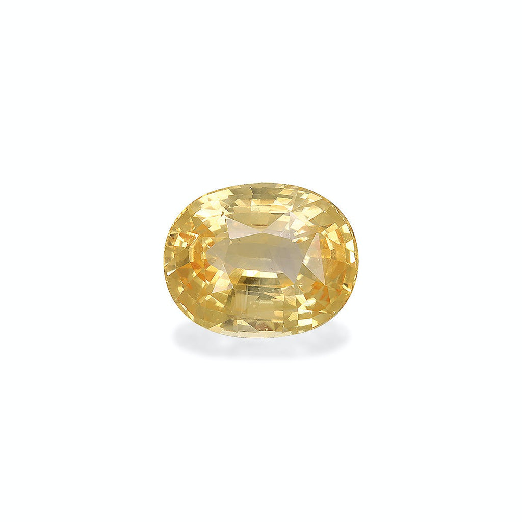 Le Saphir Jaune · 4,5ct de Bonnot Paris, une pierre précieuse jaune de forme ovale avec une surface facettée, reflète magnifiquement la lumière et rayonne d'une lueur brillante sur un fond blanc uni.