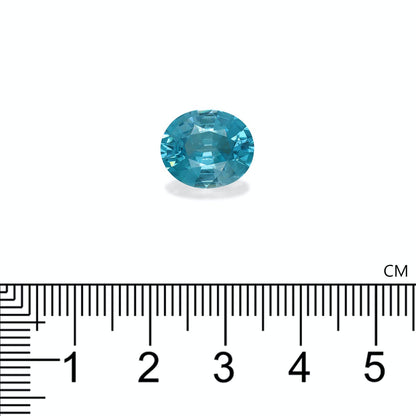 La pierre précieuse Zircon Bleu de 7,65 carats de Bonnot Paris, une gemme bleue ovale mesurant environ 1,8 cm de large, repose sur un fond clair avec des repères de règle en centimètres visibles en dessous.