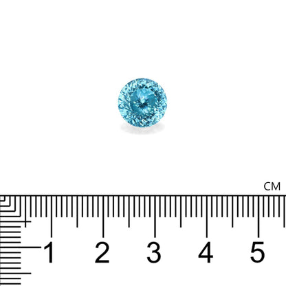 Une pierre précieuse Zircon Bleu · 7,56 ct de Bonnot Paris, de forme petite et ronde, est présentée sur un fond blanc à côté d'une règle centimétrique noire, soulignant son diamètre approximatif de 1 centimètre.