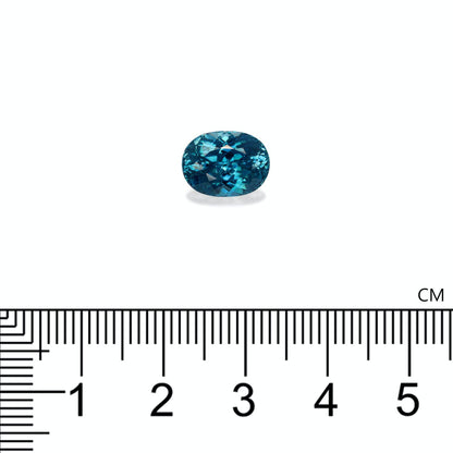Une pierre précieuse Zircon Bleu · 6,12 ct de Bonnot Paris, présentant un design sarcelle de taille ovale, est présentée sur un fond blanc à côté d'une règle centimétrique indiquant sa taille de moins d'un centimètre de longueur.